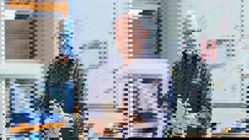 A Welltec employee smiling and holding a notebook inside a workshop or production facility, representing the company’s positive and professional work environment.